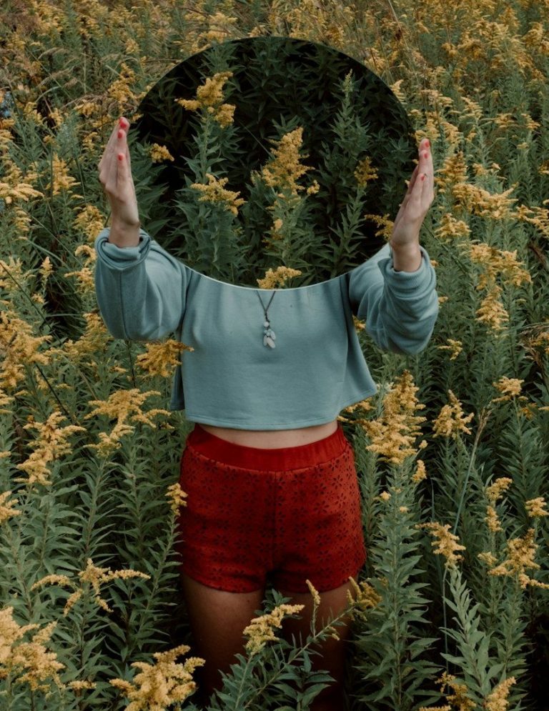 Person mit runden Spiegel in einem Blumenfeld mit gelben Blumen.