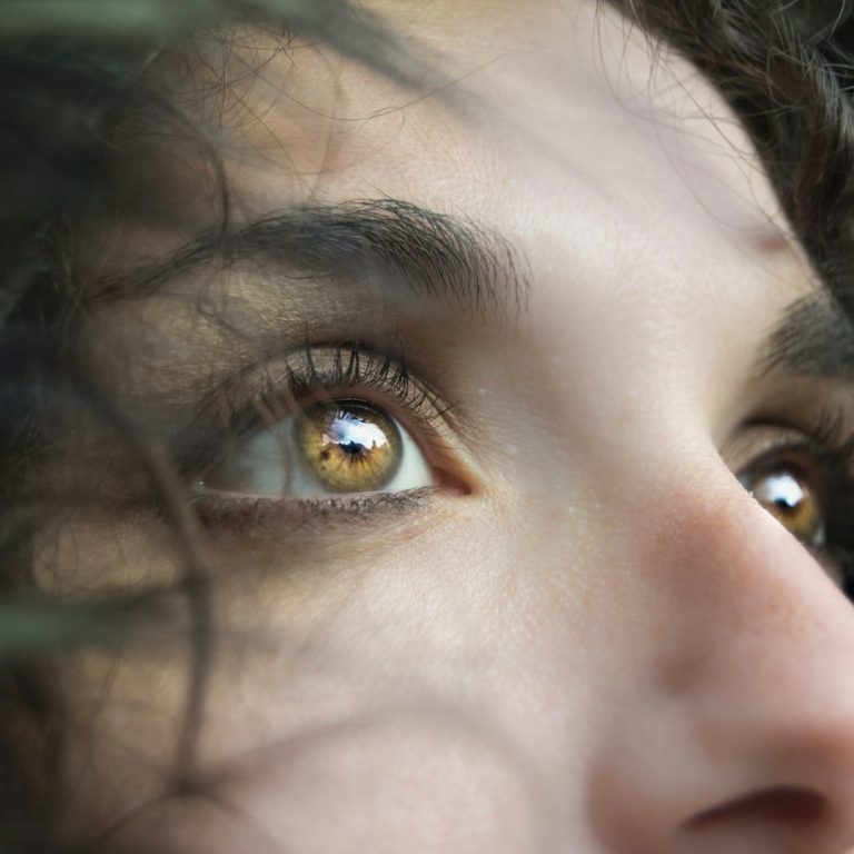 Nahaufnahme von menschlichen Augen mit grün-goldenen Iris und langen Wimpern.