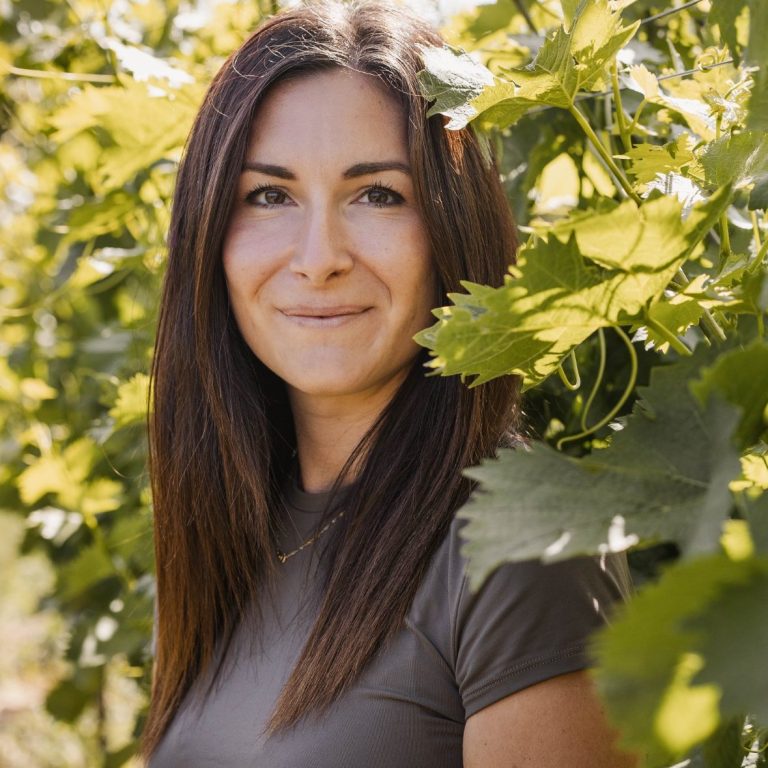 Katharina Schmitd-Hassankhani steht zwischen Weinreben und lächelt freundlich.