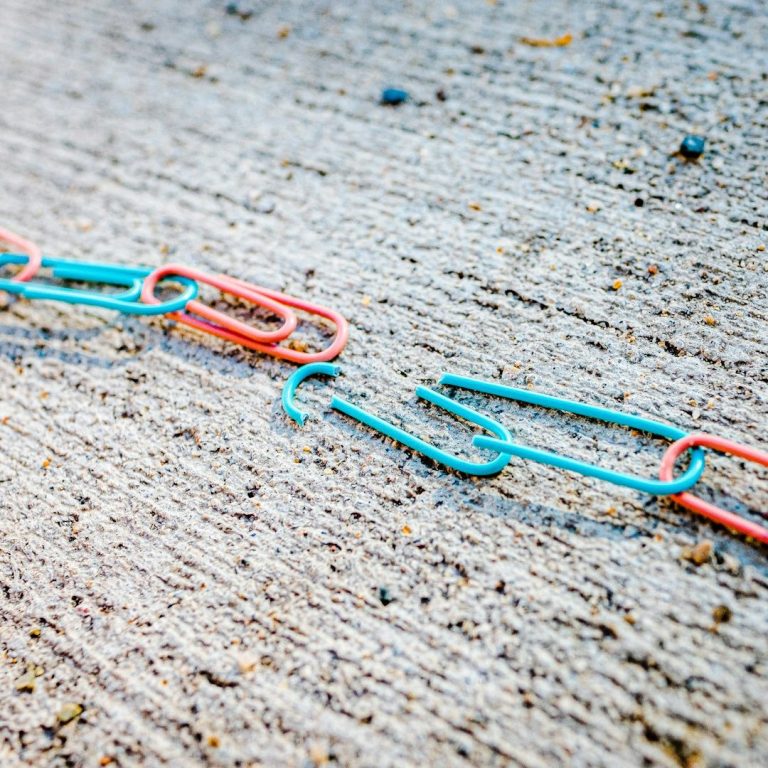 Eine zerbrochene Kette aus Büroklammern auf grauem Hintergrund.