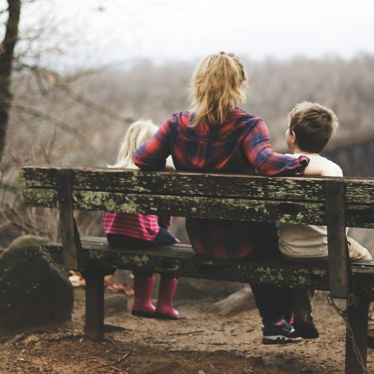 Eine Frau sitzt mit zwei Kindern auf einer Bank, Blick auf die Landschaft.