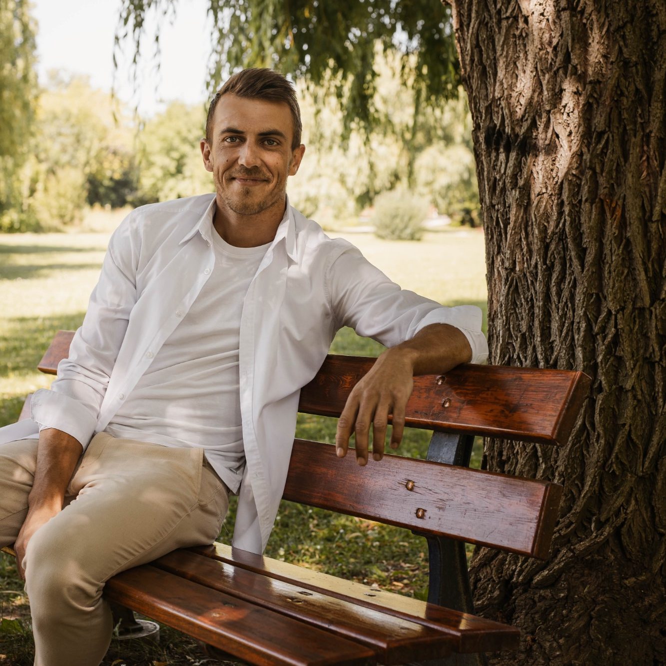Benjamin Feurer sitzt entspannt auf einer Bank unter einem Baum in einem Park.